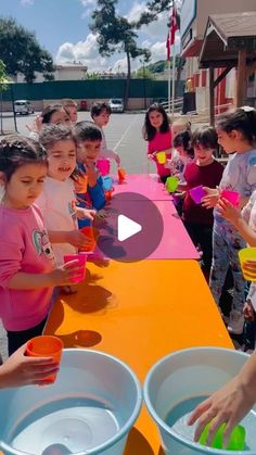 a group of children standing around a table filled with bowls and cups on top of it