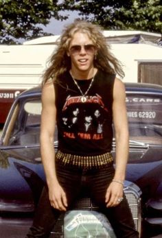 a man with long hair and sunglasses standing in front of a car