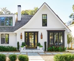 a white house with black shutters and two large windows on the front door is surrounded by greenery