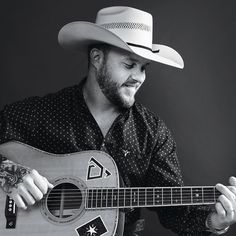 a man wearing a cowboy hat holding a guitar and playing the ukulele with his right hand