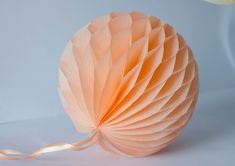 an origami ball on a white table with a flower in the corner and ribbon