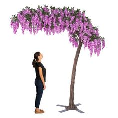 a woman standing next to a tree with purple flowers