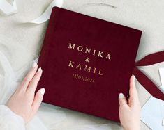 a person holding a red book on top of a white table with ribbon around it