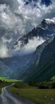 the road is empty and there are clouds in the sky over the mountain range behind it