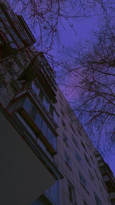 an apartment building with trees in the foreground and blue sky above it at dusk