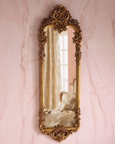 an ornate gold framed mirror on a pink wall