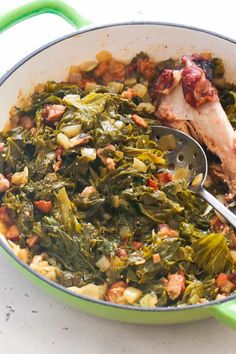 a green pot filled with greens and meat on top of a white counter next to a spoon