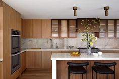 a modern kitchen with marble counter tops and wooden cabinets, along with black bar stools