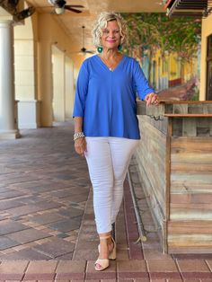 a woman standing in front of a bar wearing white pants and a blue top with her hands on her hips