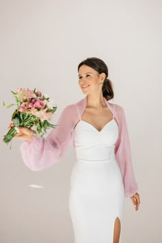 a woman in a white dress and pink cardigan holding a bouquet of flowers with her right hand