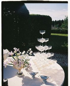 there are many wine glasses on the table with flowers in vases next to it