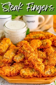 some fried fingers are on a wooden plate with dipping sauces in the back ground