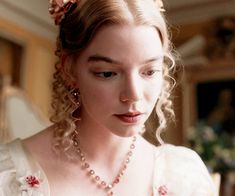 a woman in a white dress is looking down at her cell phone while wearing a flowered necklace