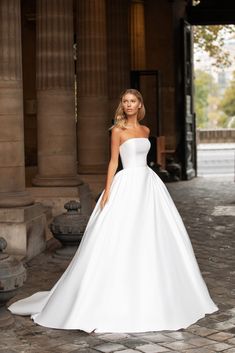 a woman in a white wedding dress standing on a stone walkway with columns behind her