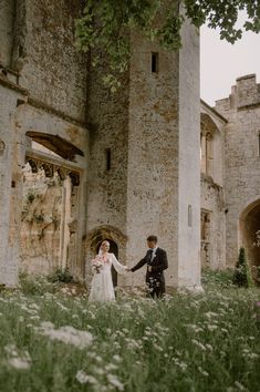 a bride and groom holding hands in front of an old castle with stone walls, grass and flowers