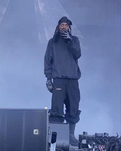 a man standing on top of a stage with his hands in his ears and holding a cell phone to his ear