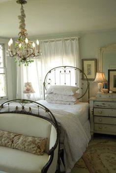 a white bed sitting next to a window in a bedroom under a chandelier