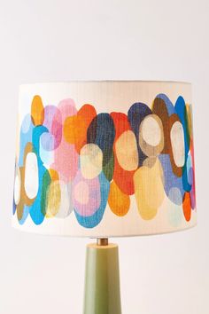 a colorful lamp shade on a table with a green base and white lampshade