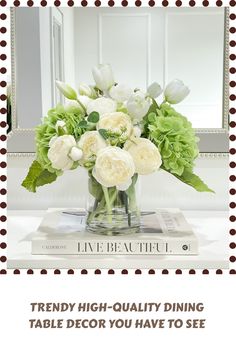 a vase filled with white flowers sitting on top of a table next to a mirror