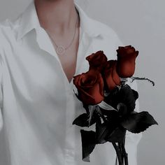 a woman wearing a white shirt holding two red roses in her hand and a necklace on her neck