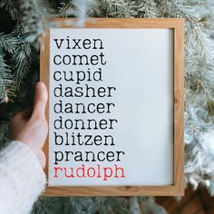 a person holding up a cross stitch pattern in front of a christmas tree with the words vixen, comet, dasher, dancer, dancer, biltzen, prae