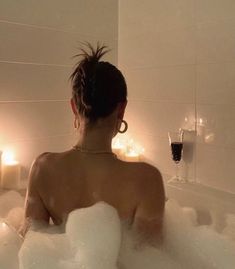 a woman sitting in a bathtub with candles around her