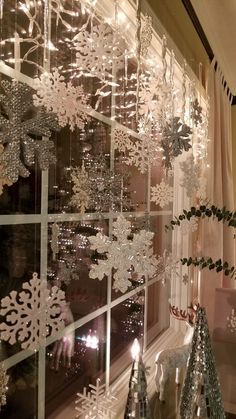 a window with snowflakes hanging from it's side and christmas decorations on the windowsill