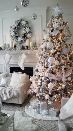 a white christmas tree in a living room decorated with silver ornaments and stockings on the mantle