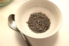 a white bowl filled with lavender sprinkles next to a silver spoon on a table