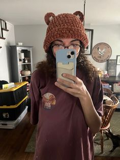 a woman taking a selfie with her cell phone wearing a knitted bear hat