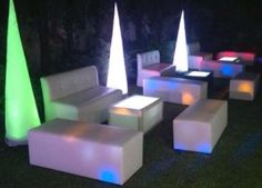 an outdoor seating area is lit up at night with colorful lights on the benches and tables