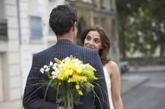 a man in a suit holding a bouquet of flowers next to a woman wearing a white dress