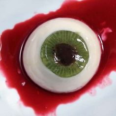 an eyeball with a green center surrounded by blood on a white surface, in the shape of a human eye