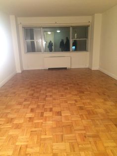 an empty room with hard wood flooring and two people standing in the window sill