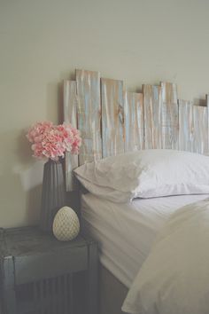 a bed with white linens and pink flowers in a vase