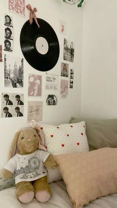 a teddy bear sitting on top of a bed next to a pillow and a record