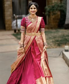 a woman in a pink and gold sari is walking down the street with her hand on her hip