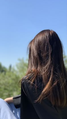 the back of a woman's head as she sits on a bench with trees in the background