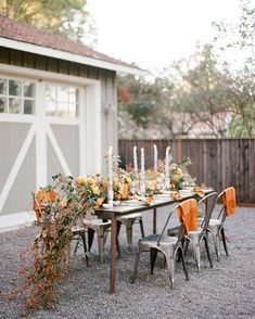 an outdoor dining table with candles and flowers on it in front of a garage door