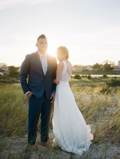 a bride and groom standing in the sand at sunset