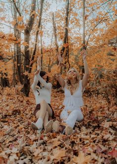 two people sitting on the ground with their arms in the air and leaves all around them