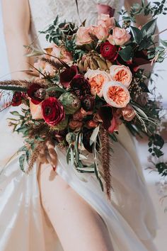 a bride holding a bouquet of flowers and greenery on her wedding day at the same time