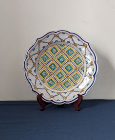 a decorative plate sitting on top of a blue floor next to a white wall and wooden stand