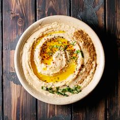 a white bowl filled with hummus on top of a wooden table