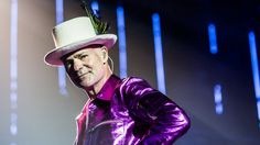 a man in a purple jacket and hat on stage