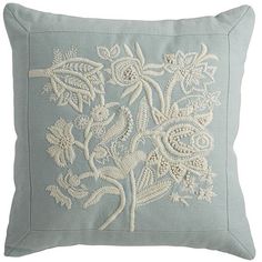 a light blue pillow with white embroidered flowers on the front and back, sitting on a white background