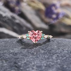 a pink heart shaped diamond ring on top of a rock