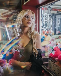 a woman wearing glasses standing in front of a window with stuffed animals on it's sides