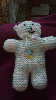 a crocheted white teddy bear sitting on top of a purple bed sheet next to a wooden chair