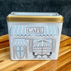 a blue and white container with an image of a cafe on the front, sitting on top of a wooden table